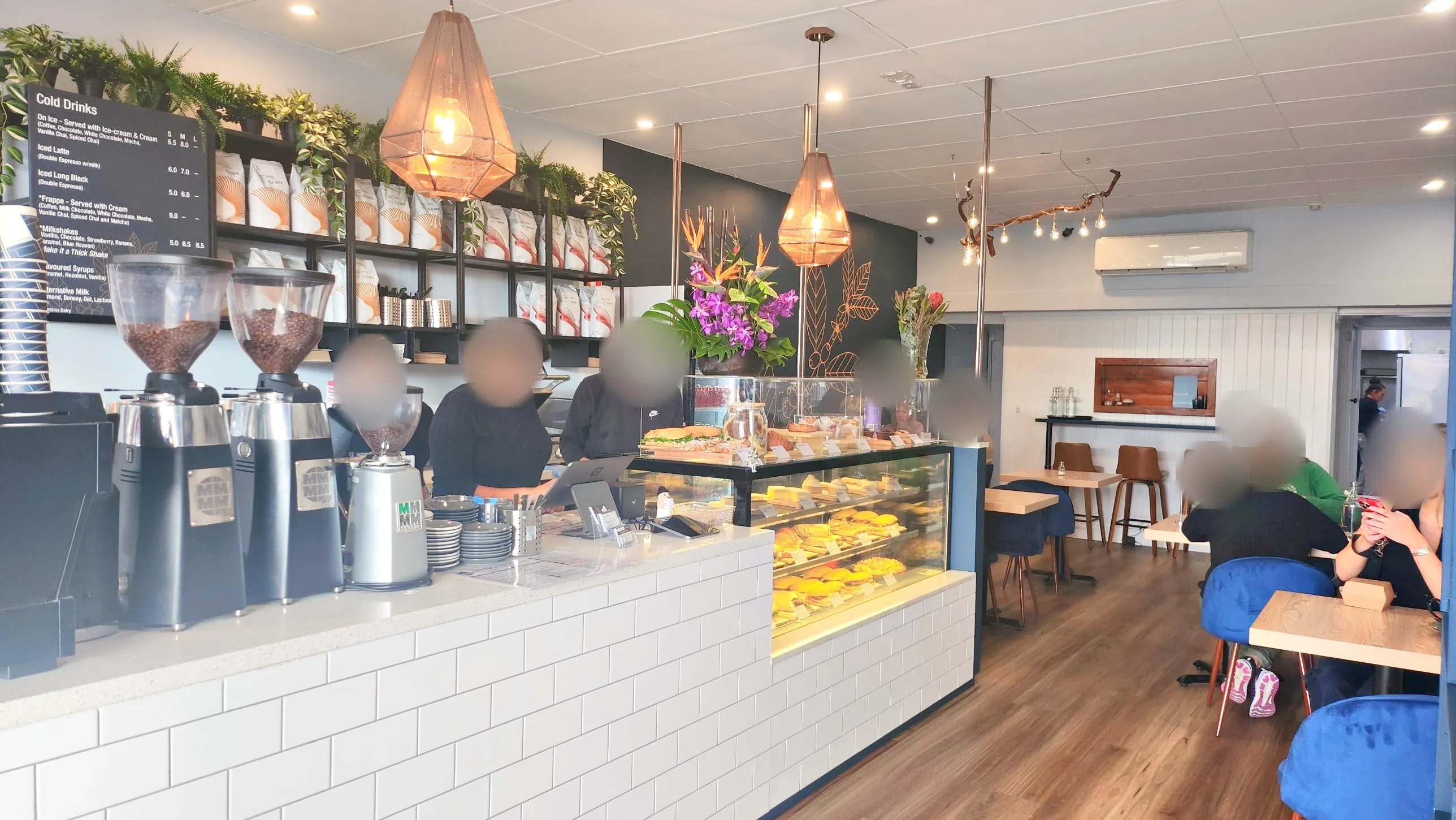 Inside the Melbourne café: the counter, coffee grinders and cabinet, with customers at the tables.